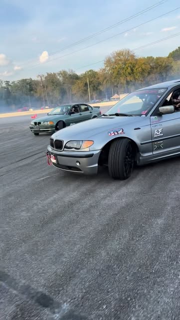Two BMW E46s drifting in tandem with tire smoke on track